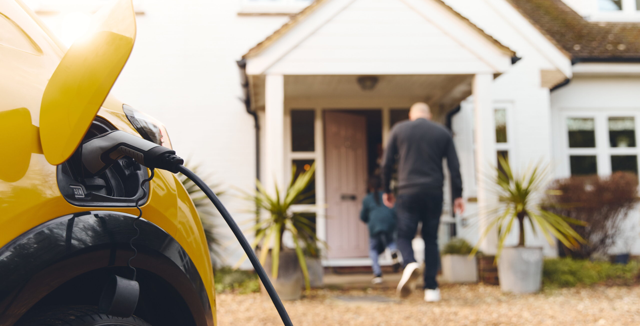 A yellow car which is plugged into an EV charging point which has been installed by someone currently living in this house.